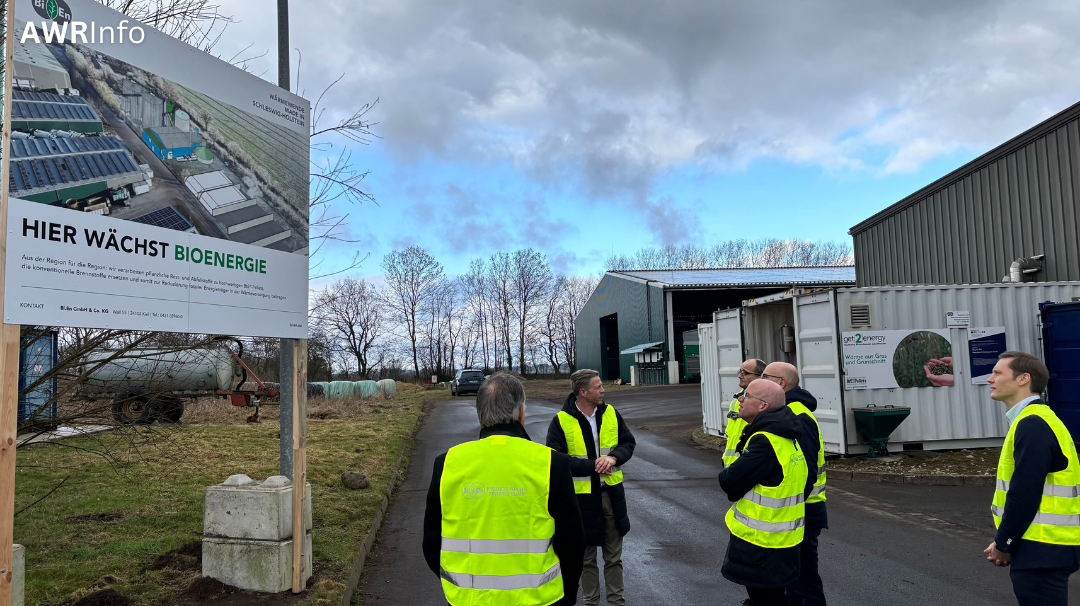 Personen stehen vor Infotafel mit dem Satz "Hier wächst Bioenergie"